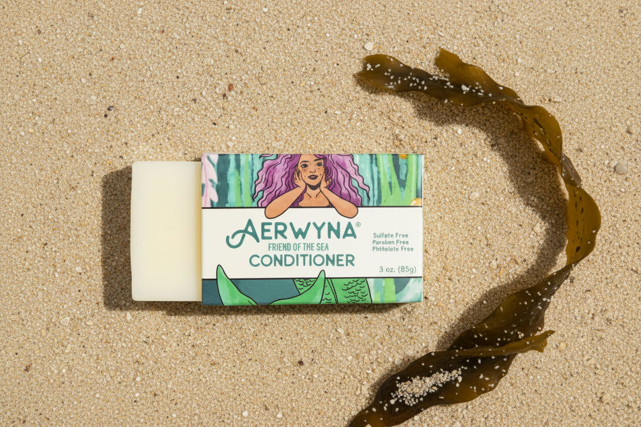 Aerwyna solid conditioner bar resting in sand with seaweed — plastic-free, sulfate-free haircare