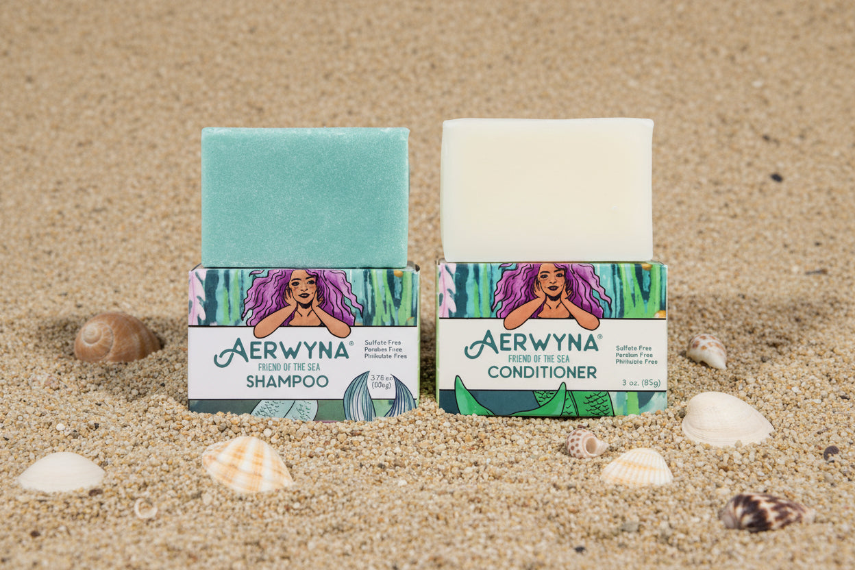 Aerwyna complete set — solid shampoo bar and conditioner bar resting in sand with sea shells