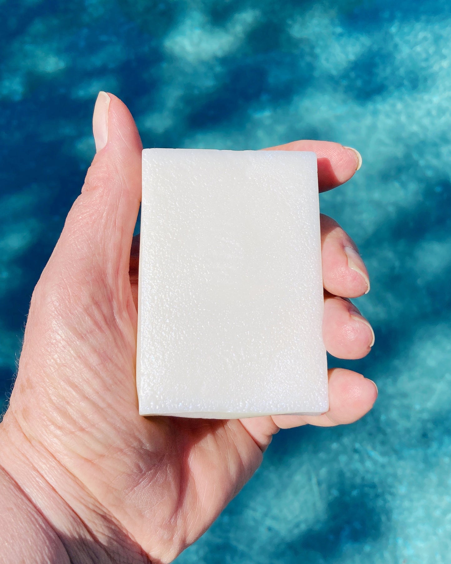 Aerwyna solid conditioner bar held in hand against blue water background- concentrated plastic-free conditioning